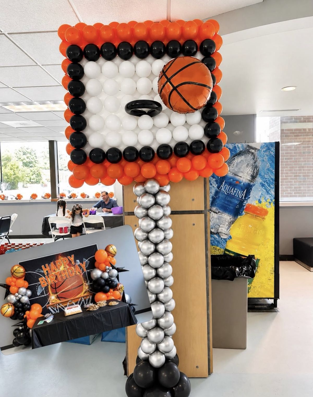 A basketball hoop built entirely from orange, black, white and chrome silver balloons, taller than a person