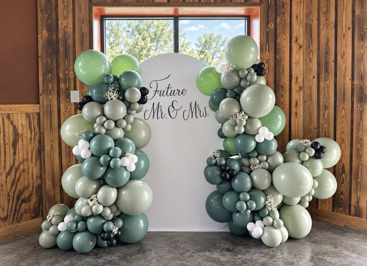 Sage, eucalyptus and white balloon garlands with baby's breath around a white arch reading Future Mr and Mrs
