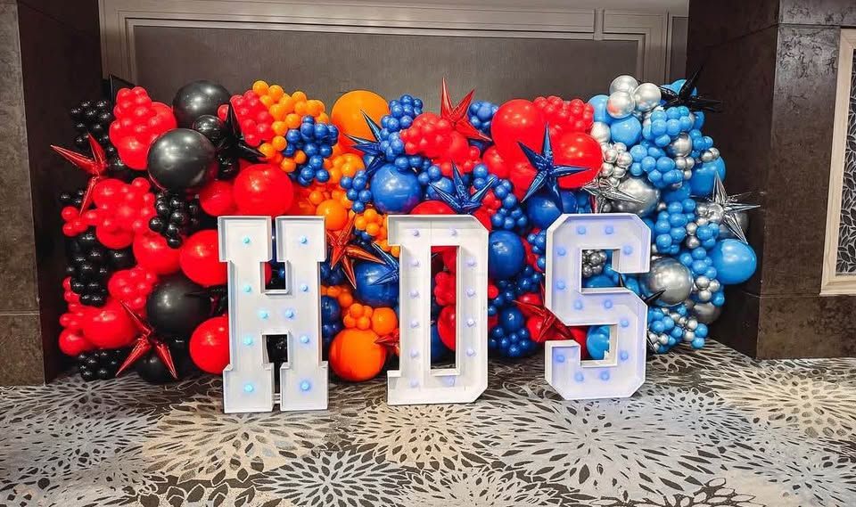 Red, black, orange, blue and silver balloon wall behind lit marquee letters H D S