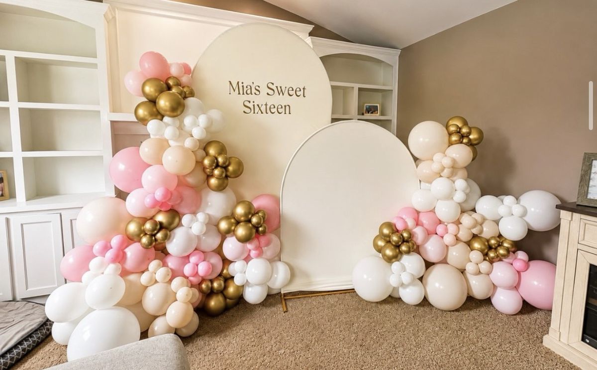 Pink, blush, white and chrome gold balloon garlands around two cream arches reading Mia's Sweet Sixteen in a living room