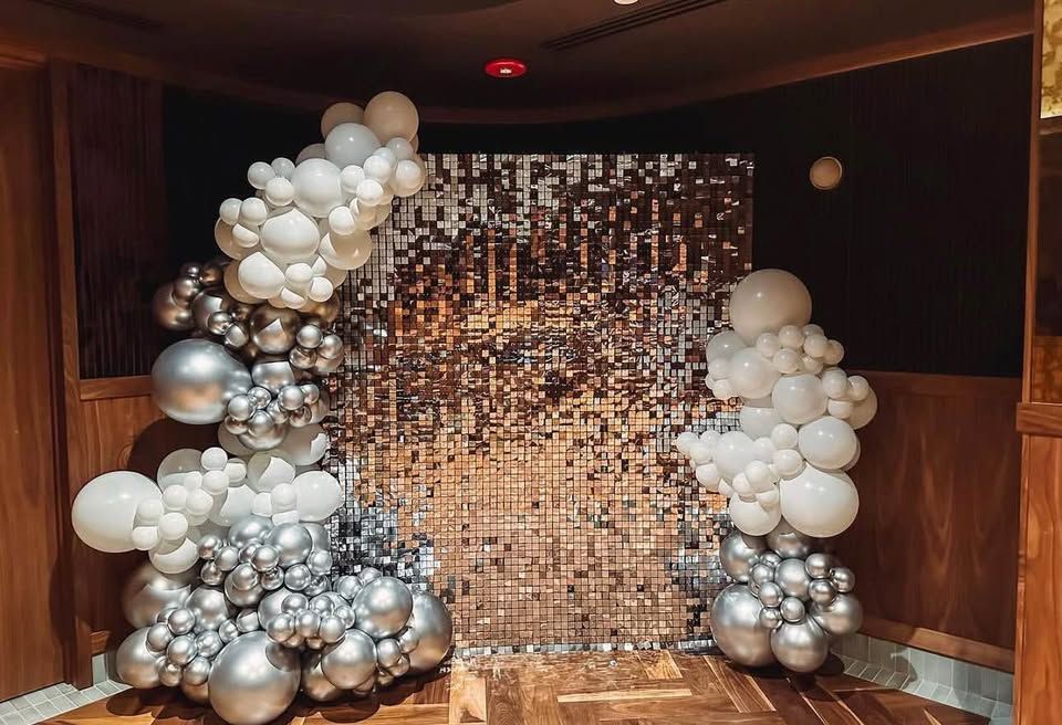 White and chrome silver balloon garlands on both sides of a silver sequin wall in a wood-paneled room